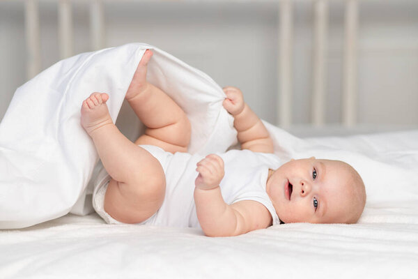 happy baby on the bed in the morning. Textiles and bed linen for children. A newborn baby has woken up or is going to bed