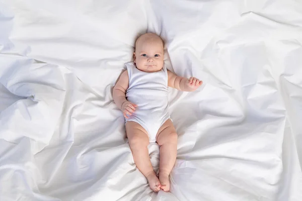 a child on a white bed in the morning. Textiles and bed linen for children. A newborn baby has woken up or is going to bed