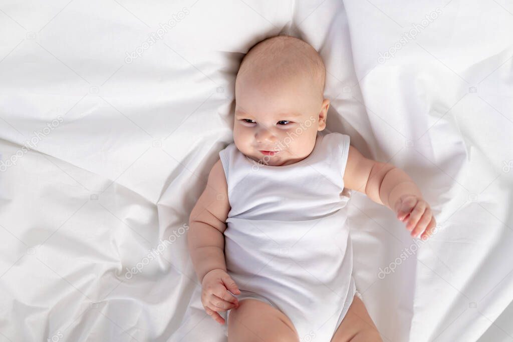 portrait of a child on a white bed in the morning. Textiles and bed linen for children. A newborn baby has woken up or is going to bed