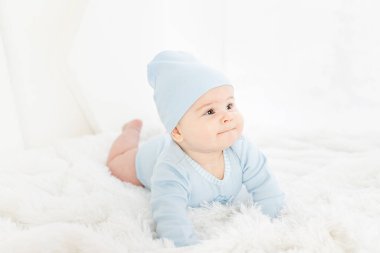 Mavi elbiseli bir bebek beyaz halıda karnının üstünde yatıyor.