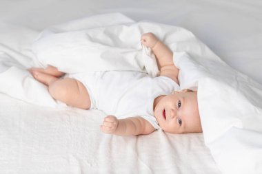 Sabahları yatakta mutlu bir bebek. Çocuklar için tekstil ve çarşaf. Yeni doğmuş bir bebek uyandı ya da yatmaya gidiyor.