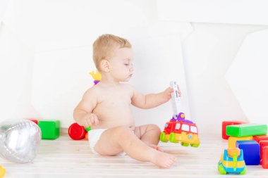 Küçük bir çocuk. Altı aylık bir çocuk. Parlak beyaz bir odada parlak oyuncaklarla oynuyor.