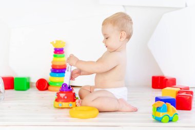 Küçük bir çocuk. Altı aylık bir çocuk. Parlak beyaz bir odada parlak oyuncaklarla oynuyor.