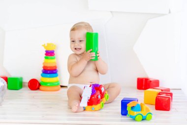 Küçük bir çocuk. Altı aylık bir çocuk. Parlak beyaz bir odada parlak küplerle oynuyor.