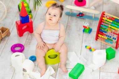 Bebek tuvalette işiyor ve evdeki çocuk odasında tuvalet kağıdıyla oynuyor.