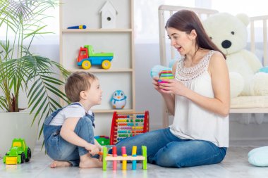 Anne, çocuk odasında eğitici oyuncaklar oynayarak çocuğa evde ders veriyor. Mutlu, sevgi dolu bir aile..