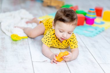 Bebek çocuk, çocuk odasında parlak renkli oyuncaklarla sarı bir vücutla oynuyor.
