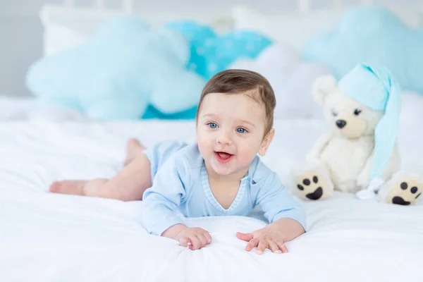 smiling or laughing baby on the bed to sleep with teddy bear, baby room interior, healthy happy little baby