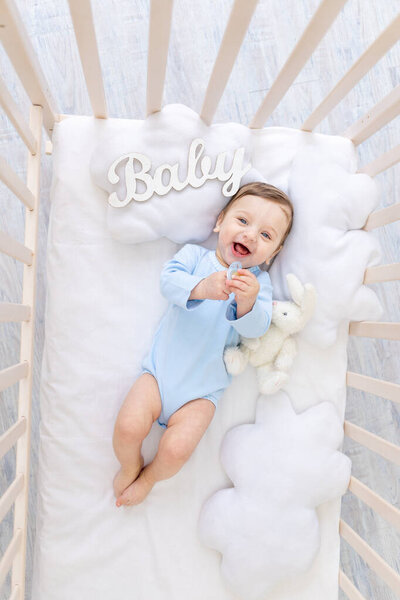 happy smiling baby boy in the crib with the inscription baby in a blue bodysuit, cute joyful little baby in the bedroom