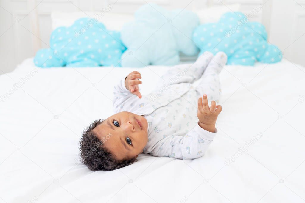 African-American little child on a white bed in the bedroom is lying in pajamas
