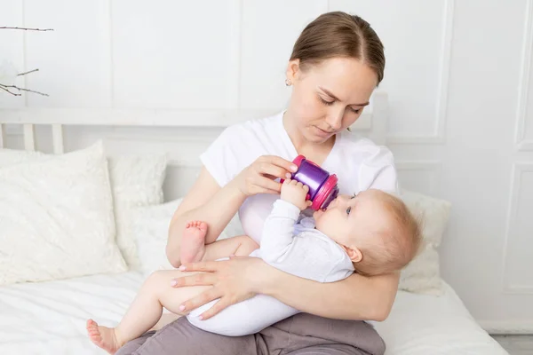 mom drinks or bottle feeds a baby on a white bed at home, baby food concept