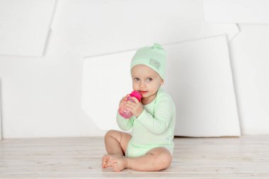 Bebek, yeşil tulumlu bir şişeden içer. Beslenme ve bebek maması konsepti.