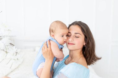 Yeni doğmuş bebeği olan genç anne evde yatakta sarılıyor, mutlu aile ve doğum günü konsepti.