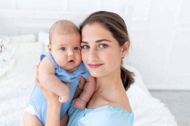 Yeni doğmuş bir bebeği olan genç bir anne onu evde, yatakta nazikçe kucaklıyor. Mutlu bir aile ve doğum kavramı.