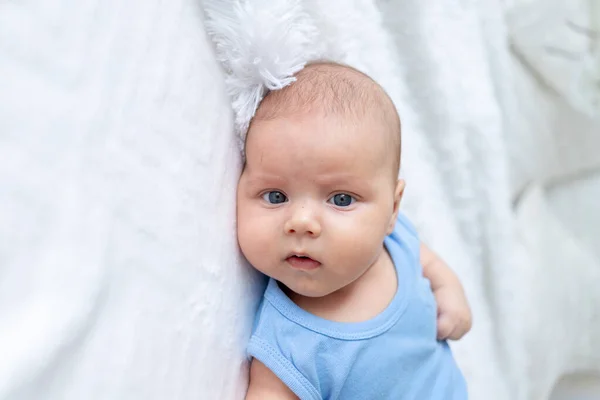 照片上的一个可爱的男婴 三个月大 穿着蓝色的紧身衣 躺在家里的一张白色床上 — 图库照片
