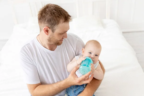 dad feeds baby son from a bottle at home, happy fatherhood, baby food concept