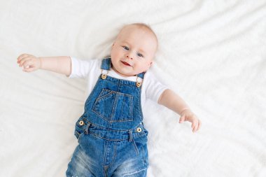 Evde beyaz bir yatakta kot takım elbiseyle yatan sevimli bebek gülüşleri.