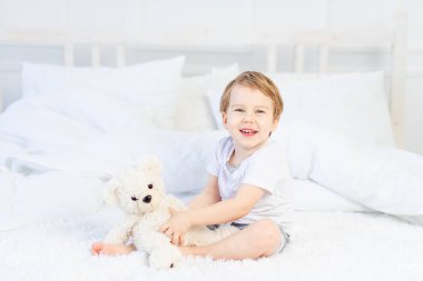Evde yatağında oyuncak ayıyla oynayan ve gülen bir çocuk.