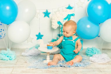 Bebek doğum günü pastası yer ve ilk doğum gününü kutlar. Mavi renkli, balonlu ve pastalı fotoğraf bölgesinde.