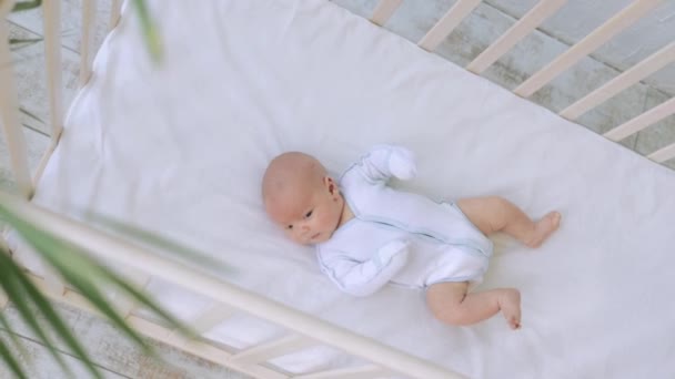 Ένα νεογέννητο μωρό ξυπνάει ή παίζει στην κούνια. Υπέροχο καυκάσιο αγοράκι, ξαπλωμένο στο πάνω κρεβάτι. Η έννοια της φροντίδας των παιδιών και της γονικής αγάπης — Αρχείο Βίντεο