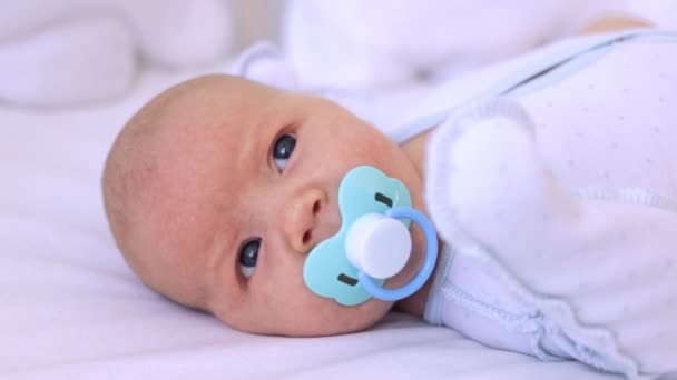 Portrait of a newborn baby with a pacifier. Beautiful Caucasian little baby boy lying on the bed. The concept of birth and child care — Stock Video