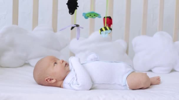 Cute little newborn baby playing mobile in white bed before going to bed, toddler with toys — Stock Video