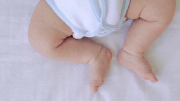 The feet of a small child lying in a crib on a white cotton bed at home close-up, the heels of a newborn sleeping baby — Stock Video