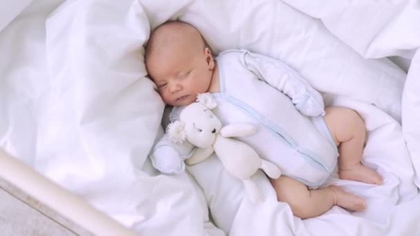 Słodkie mały noworodek chłopiec śpi w żłobku na białym bawełnianym łóżku w domu z zabawką w ręku, zdrowy sen dziecka — Wideo stockowe