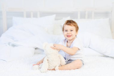 Evde yatağında oyuncak ayıyla oynayan ve gülen bir çocuk.