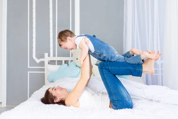 En lycklig, kärleksfull familj. Mamma och lille son leker hemma på sängen, har kul och skrattar — Stockfoto