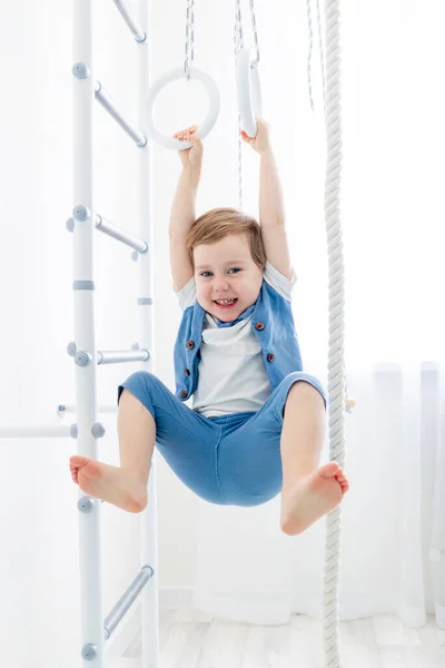 Un niño en la pared sueca practica deportes en casa, un niño sube una escalera con una cuerda, el concepto de deporte y salud — Foto de Stock