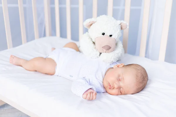 新生儿在卧室的婴儿床里健康地睡觉，床上躺着一只柔软的玩具熊 — 图库照片