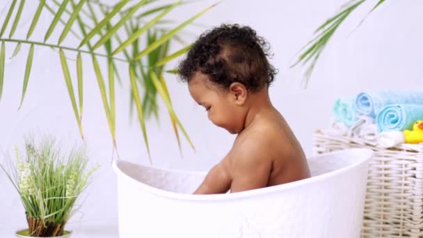 Американо-африканский мальчик купается в ванне с пеной и играет с водой, концепция гигиены и ухода за детьми — стоковое видео