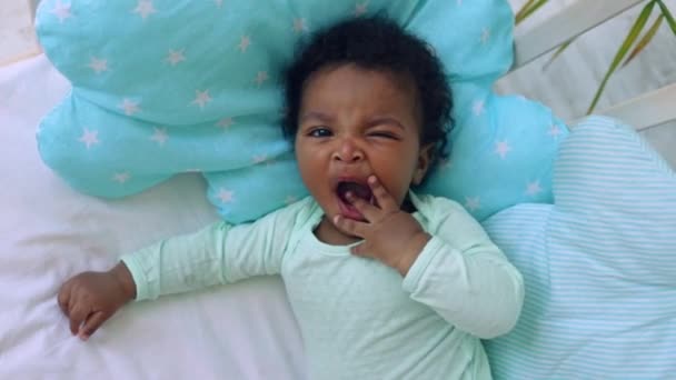 Un niño bostezo americano-africano yace en la cama sobre una cama de algodón azul — Vídeos de Stock