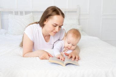 Annem evde pamuklu yatak ile beyaz bir yatakta yatmadan önce bebeğe kitap okur, mutlu bir ailedir..