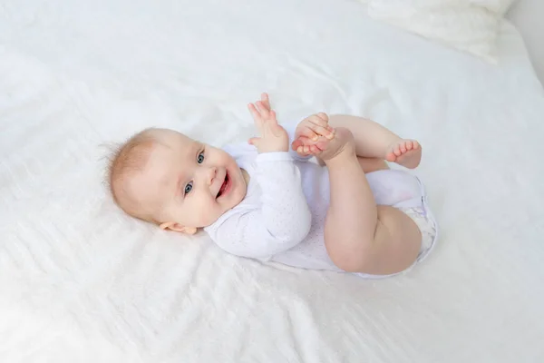 Smiling Baby Girl Six Months Old Plays Her Legs Lying — Stock Photo, Image