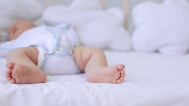 The feet of a small child lying in a crib on a white cotton bed at home, the heels of a newborn baby — Stock Video