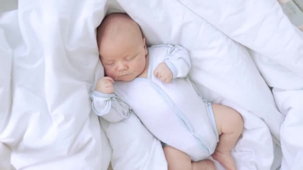 Cute little newborn baby boy sleeps in the nursery on a white cotton bed at home — Stock Video