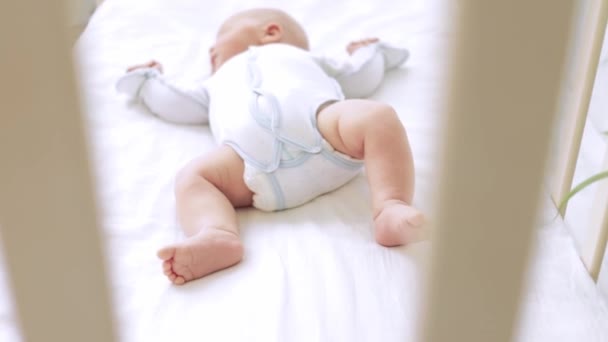 Nohy malého dítěte, které leží v postýlce na bílé bavlněné postýlce zblízka doma, podpatky novorozence spícího — Stock video