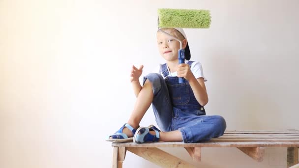 Un niño con un rodillo en las manos pinta las paredes o realiza trabajos de construcción molar en la pared blanca del apartamento — Vídeo de stock