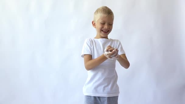 Menino sorri e lava as mãos com sabão e espuma em um fundo branco isolado, espaço para texto — Vídeo de Stock