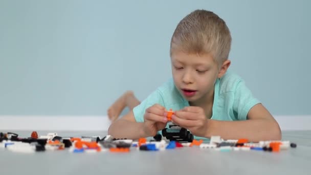 Un enfant garçon recueille avec enthousiasme un constructeur sur le sol de petites pièces, le développement et les loisirs des enfants d'âge préscolaire — Video