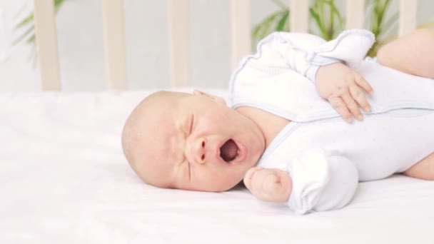 Ett gäspande nyfött barn i en barnsäng på en bomullssäng hemma har vaknat eller somnar — Stockvideo