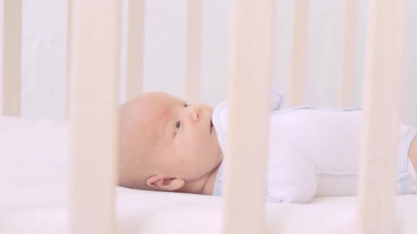Um bebê recém-nascido em um berço em uma cama de algodão em casa está acordado ou adormecendo — Vídeo de Stock