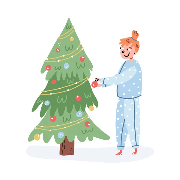 Linda escena de Nochebuena. Chica cabeza de jengibre en acogedor pijama de lunares decorando el árbol de Navidad con adornos. — Archivo Imágenes Vectoriales