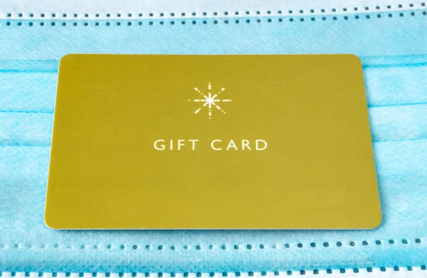 gift card with medical mask on green background. yellow gift card and blue mask. 2020 Christmas.