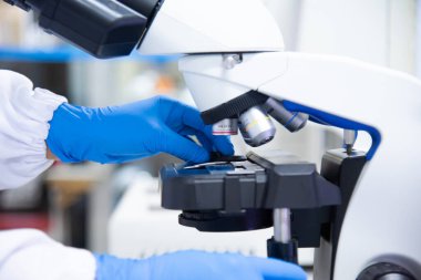 Laboratuvarda mikroskop kullanarak mavi eldivenli el bilim adamını kapat..