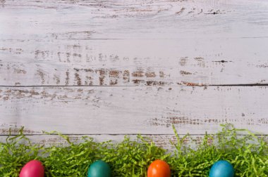 Çerçevenin altında dört renkli Paskalya yumurtası paskalya otlarının üstünde, beyaz ahşap arka planı ve kopyalama alanı var.