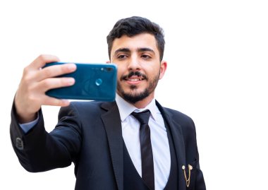 Takım elbiseli ve cep telefonuyla selfie çeken bir adam gülümseyerek ve teçhizatlı.