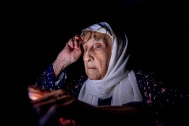 Yaşlı kadın gece yarısı karanlık odada dizüstü bilgisayarıyla çalışıyor.